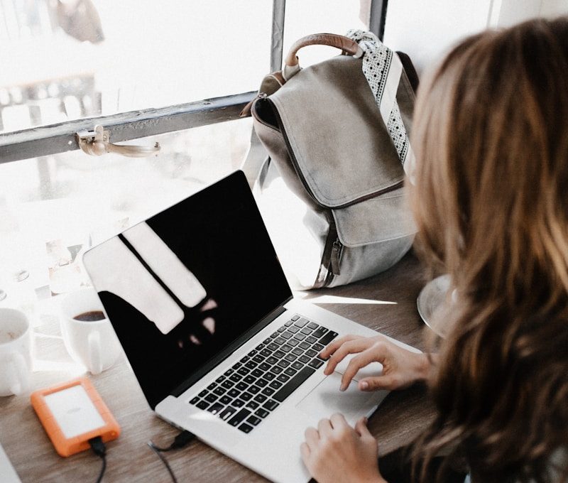girl wearing grey long-sleeved shirt using MacBook Pro on brown wooden table